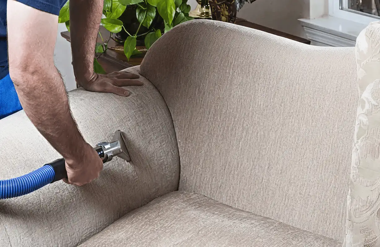 Professional upholstery cleaner deep-cleaning a fabric sofa with a handheld extraction tool and hose, Omaha, NE.